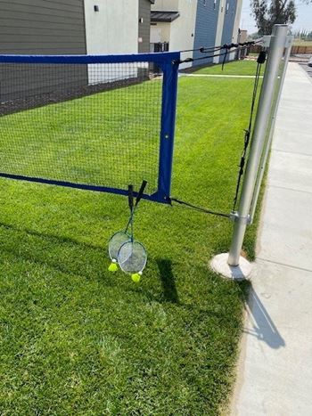 a tennis racket and two tennis balls on the grass next to a fenceat Westbury Apartments, California, 91739